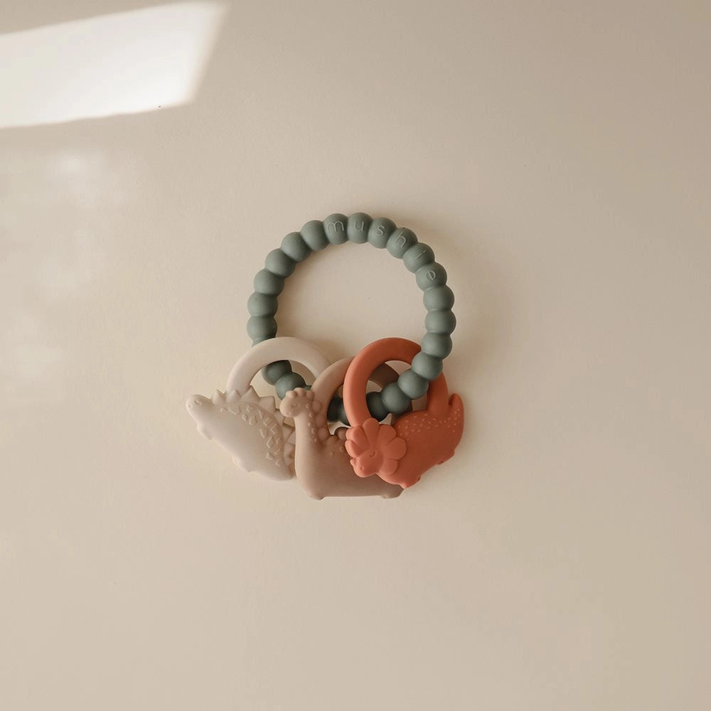 Mushie bidering Dino med dinosaurer i rolige farver – silikone bidering til baby og tandfrembrud