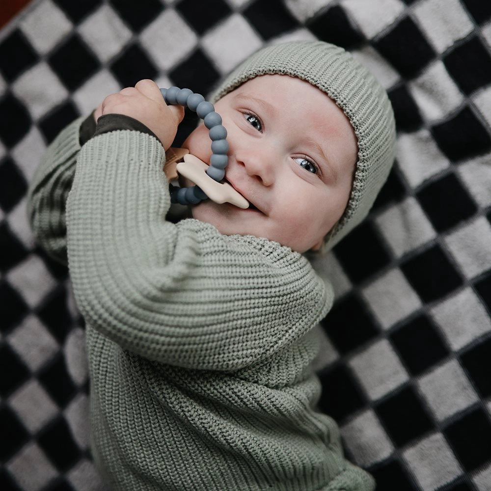 Baby iført Mushie Chunky Knit Sweater i Light Mint og Chunky Knit Beanie i Light Mint bider i Mushie bidering Space – blød silikone bidering til tandfrembrud