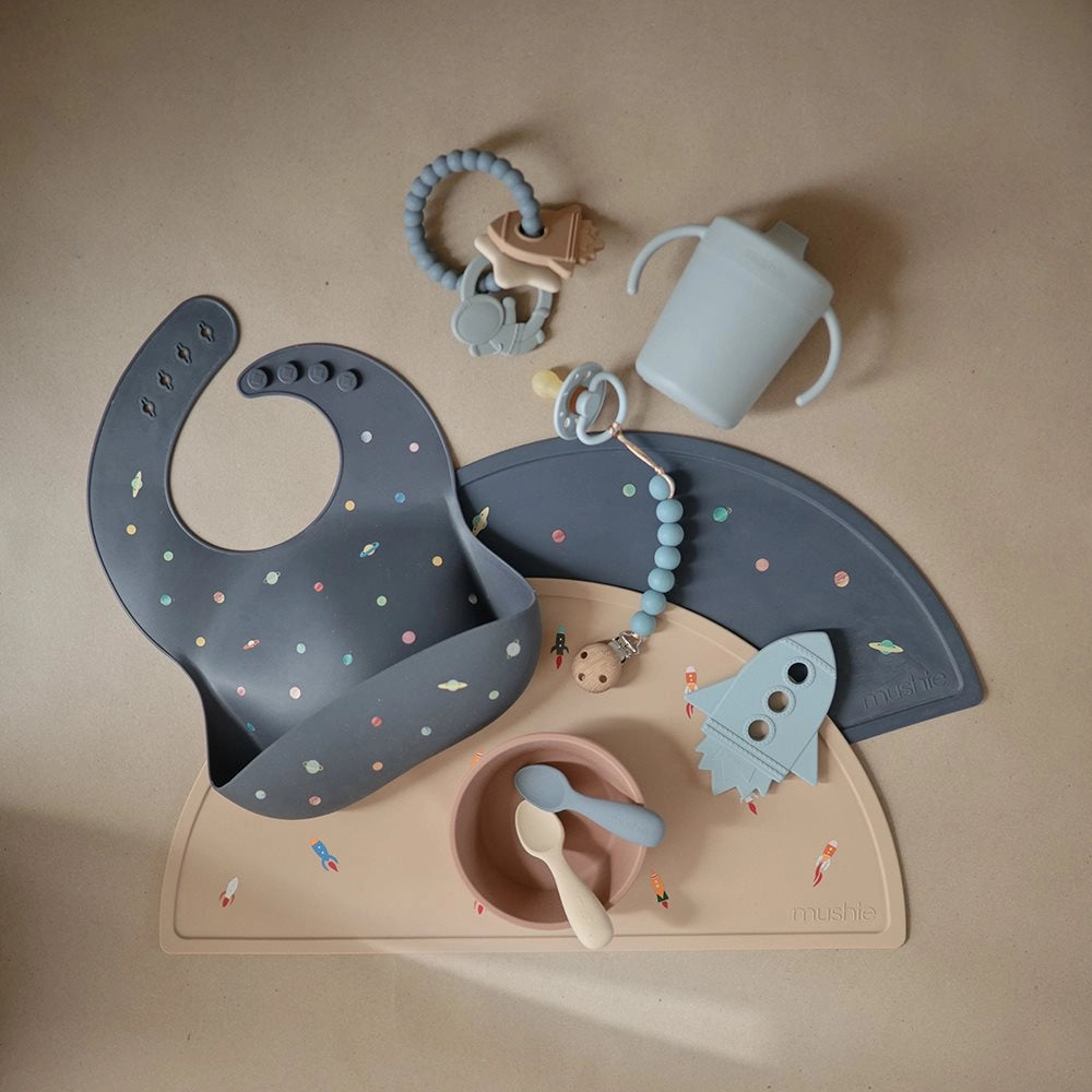 Mushie bidering Space sammen med Mushie hagesmæk i Space design, FRIGG Moon Phase sut i Powder Blue og babytilbehør