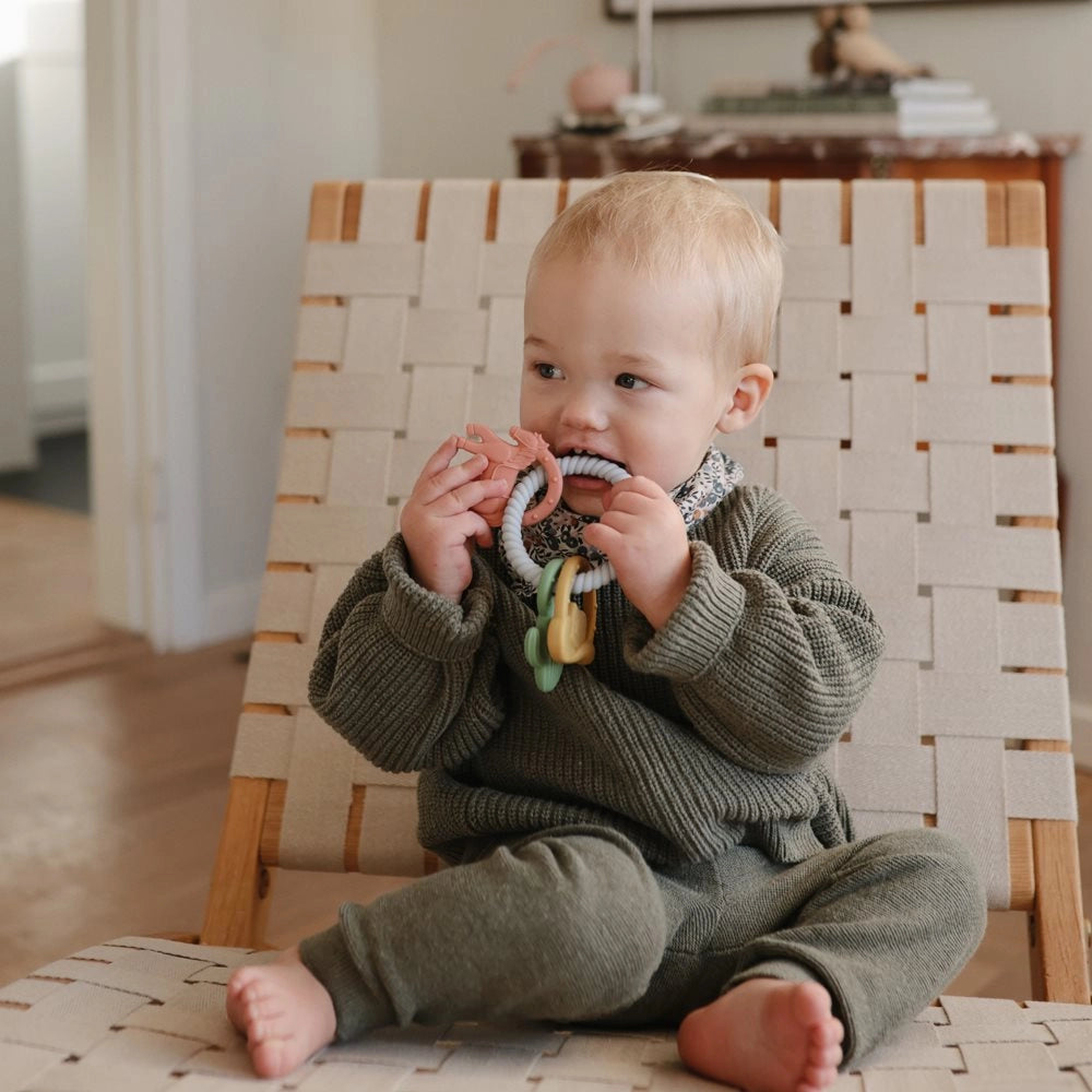 Baby iført Mushie Chunky Knit Sweater i Light Mint sidder og bider i Mushie bidering Western – silikone bidering til ømme gummer