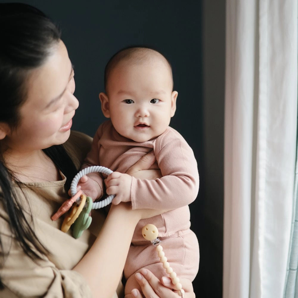 Baby iført Mushie to-delt bomuldssæt i Blush holdes og leger med Mushie bidering Western – blød bidering til tandfrembrud