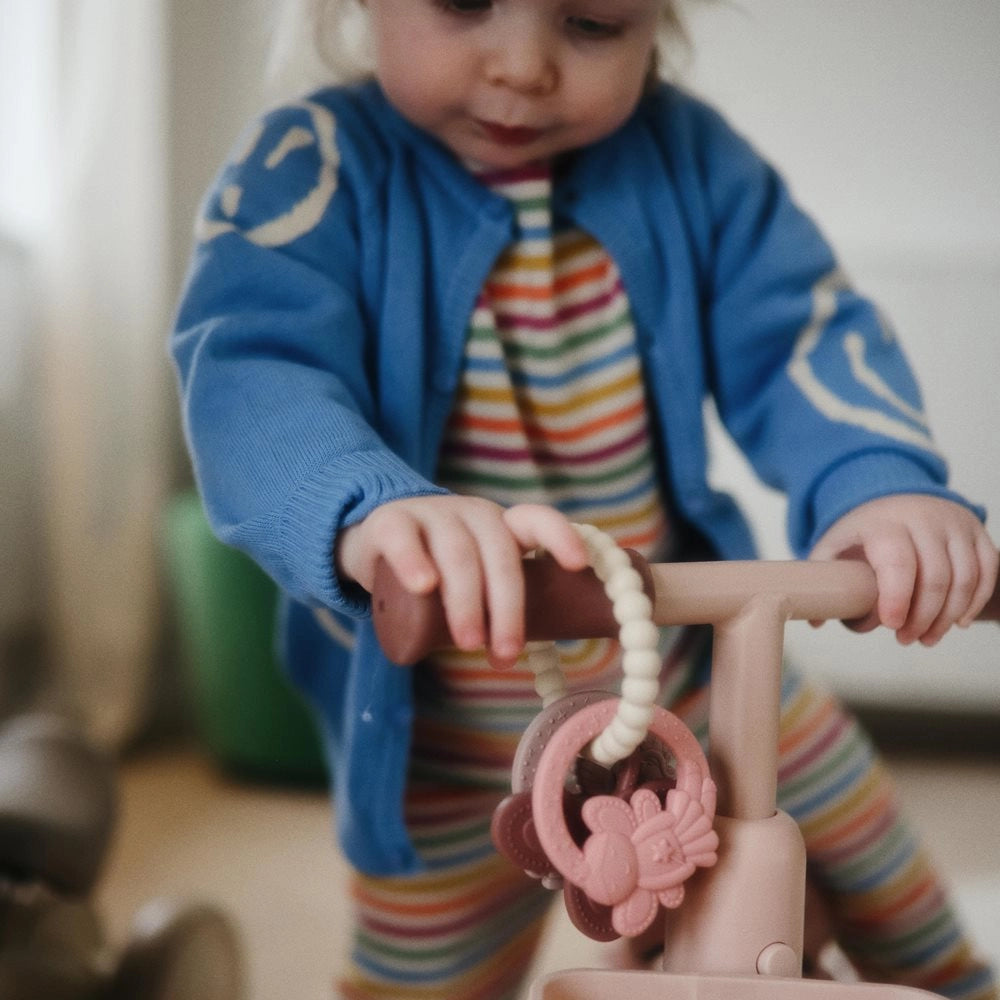 Baby på Mushie løbecykel med Mushie bidering Fairy på styret – bidering i silikone til baby og tandfrembrud